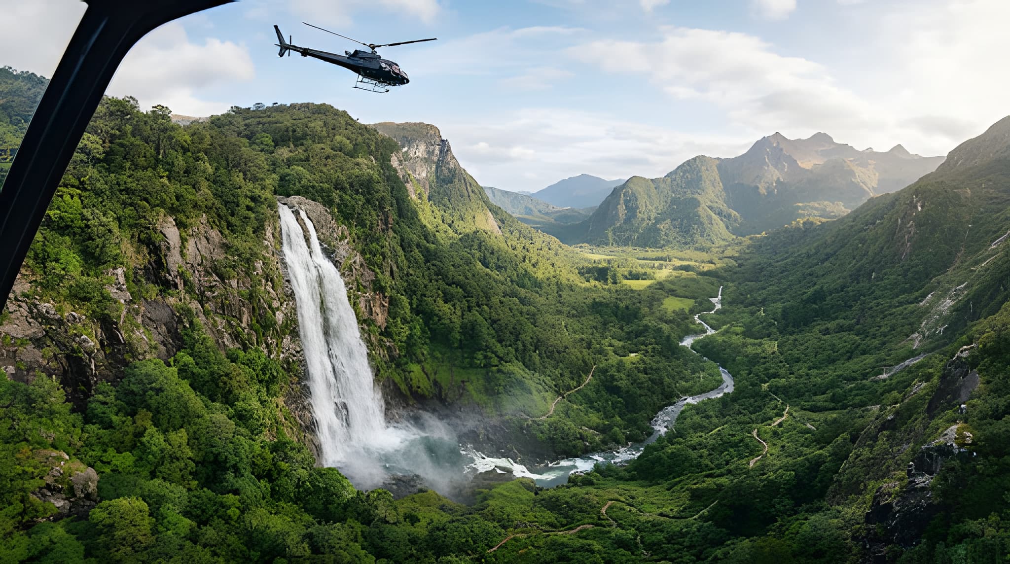 Aerial view across a waterfall and green mountain valley